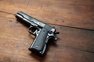 Tahta arka planda 9mm 'lik tabanca. Siyah metal silah, ordu için otomatik tabanca ve klasik bir masada güvenlik. Yan görünüm