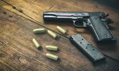 9mm 'lik tabanca ve tahta arka planda cephane mermileri. Siyah metal silah, ordu için otomatik tabanca ve klasik bir masada güvenlik. Yan görünüm
