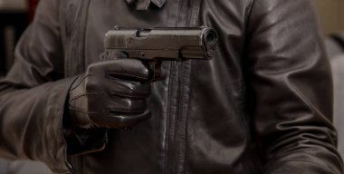 Eldivenli tabanca. Katil, siyah deri ceket giyen katil yakın çekimde bir silahla nişan alıyor. Silahlı soygun, silahlı adam kavramı.