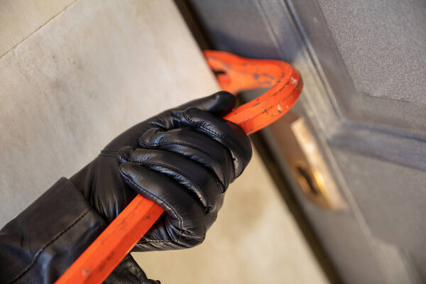 Housebreaker with crowbar. Burglar breaking a house wooden entrance door, for entering the building and stealing. Red color metal crowbar closeup view