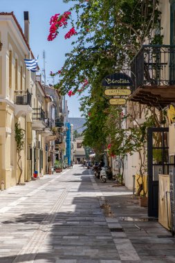 Nafplio, Moreloponnese, Argolida, Yunanistan. 27 Haziran 2021. Cobblestone Caddesi güneşli bir gün kırmızı begonviller neoklasik binalar balkonlu mimari. Yaz mevsimi Nafplion şehri. Dikey