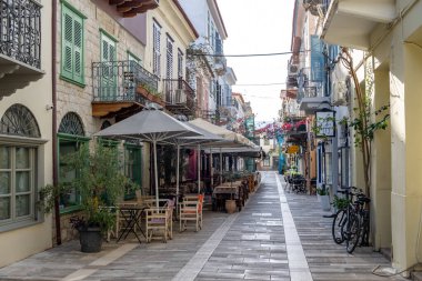 Nafplio, Moreloponnese, Argolida, Yunanistan. 28 Haziran 2021. Geleneksel kafe taverna restoranı, ahşap masalar boş sandalyeler kırmızı bougainvilleas cobblestone sokağı. Nafplion şehri turizm beldesi.