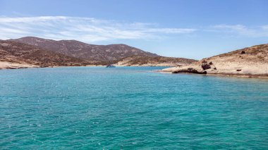 Polyaigos adası volkanik kaya oluşumları ve sahil doğası. Sakin turkuaz Ege sularında demirli lüks bir yat, berrak mavi gökyüzü, Kiklades istikameti, güneşli Yunanistan. Yaz gezisi.