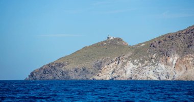 Kimolos Adası, Cyclades Yunanistan. Mavi turkuaz dalgalı Ege denizi kayalık tepesi üzerinde bina, açık gökyüzü arkaplanı. İstikamet, berrak şeffaf suyla yaz gezisi hangarı. Yüzerek rahatla. Boşluk
