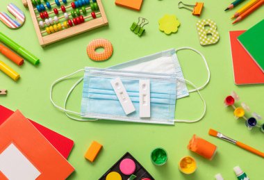 Covid 19 kendi kendine test, koruyucu tıbbi maske ve pastel yeşil arka planda okul malzemeleri, üst manzara. 2021 yılına dönersek, Coronavirus öğrencilere yönelik önleme tedbirlerini yaydı..