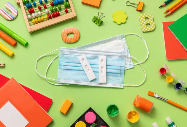 Covid 19 kendi kendine test, koruyucu tıbbi maske ve pastel yeşil arka planda okul malzemeleri, üst manzara. 2021 yılına dönersek, Coronavirus öğrencilere yönelik önleme tedbirlerini yaydı..