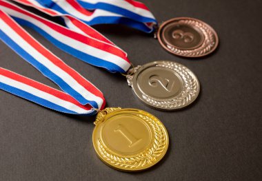 Madalyalar, altın, gümüş ve bronz. Kazananlar, Sporcular podyum ödülü konsepti. Birincilik, ikincilik ve üçüncülük ödülü siyah arka planda kırmızı mavi kurdeleye asılı..