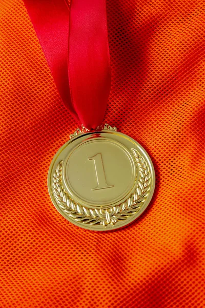 Medal gold, Winner prize award hanging with red color ribbon on athlete chest. Golden trophy in sport for first place champion on orange color shirt background