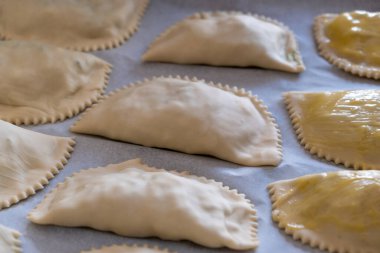 Kalitsounia pişmemiş turtalar. Bazıları pişirmek için yapışmaz kağıda yumurta sürülmüş. Pişirmeden önce kaltsounia ham hamur manzarasının üstünde. Geleneksel sağlıklı Girit yemekleri Yunan tuzlu veya tatlı atıştırmalıkları.