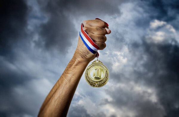 Медаль за первое место в руке спортсмена против драматического неба. Золотая награда победителя. Победа и концепция успеха