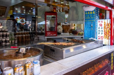 Pekin, Çin, 25 Mart 2025. Sokak yiyecekleri tezgahı canlı bir şehir pazarında eti şişledi, içkiler ve menüler sergilendi.