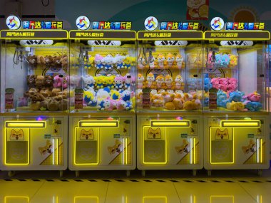 Pekin, Çin, 23 Mart 2025. Renkli pelüş oyuncaklarla dolu parlak atari makineleri bir alışveriş merkezinde neon ışıkların altında parlıyor.