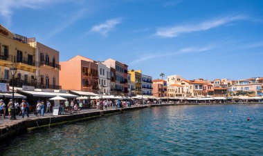 Hanya, Yunanistan, 21 Mayıs 2025. Rıhtımdaki eski Venedik liman binaları, kafelerin ve dükkanların etrafında gezinen insanlar, sakin deniz, mavi gökyüzü