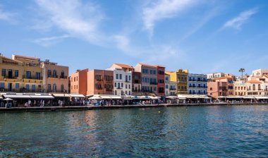 Hanya, Yunanistan, 21 Mayıs 2025. Rıhtımdaki eski Venedik liman binaları, kafelerin ve dükkanların etrafında gezinen insanlar, sakin deniz, mavi gökyüzü