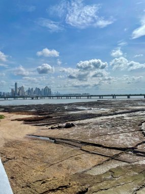 Panama City modern ufuk çizgisi ve körfezi geçen kıyı köprüsü, tropikal bir gökyüzünün altındaki alçak gelgit sırasında Casco Viejo manzarası.