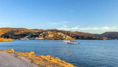 Huzurlu yelkenliler Kea 'daki Vourkari yakınlarındaki sakin mavi sularda dinleniyor, aynı zamanda Tzia olarak da bilinir, sıcak altın gün batımı ışığı altında yamaçlarda evler ve akşam güneşinde parlayan kuru arazi altında..