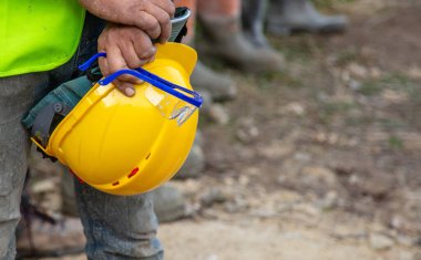 İnşaat alanında sarı güvenlik kaskı ve gözlük taşıyan işçiler güvenlik teçhizatı ve iş kıyafetlerini gösteriyor..