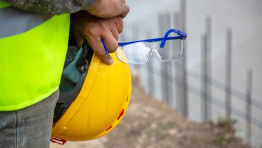 İnşaat alanında sarı başlık ve güvenlik gözlüğü takan işçiler güvenlik yeleği giyiyorlar..