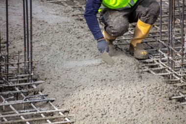 Gündüz çalışma saatlerinde inşaat sahasında ıslak beton temel döşeyen güvenlik ekipmanı işçisi.