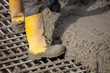 İnşaat işçisi sarı çizmeli ıslak beton döşeyen inşaat işçisi güpegündüz inşaat sahasındaki çelik inşaat demiri şebekesine..