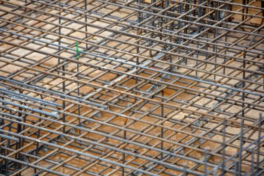 Metal demiri ızgarası, bir inşaat sahasında beton bir temeli oluşturur. Gün ışığında toprak tonları ve geometrik hassasiyetle incelenir..