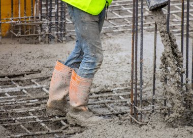 İnşaat alanında güvenlik botları ve ceketli ıslak beton döken işçiler, yakın görüş..