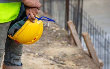 İnşaat alanında güpegündüz toprak ve metal çitli sarı miğfer ve güvenlik gözlüğü taşıyan işçiler..