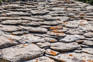 Yıpranmış taş çatı levhaları parlak gün ışığında turuncu liken ile pürüzlü katmanlı bir doku oluşturuyor.