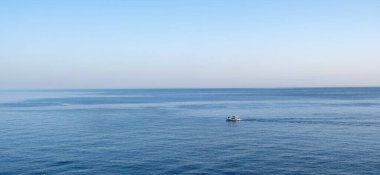 Küçük balıkçı teknesi berrak gökyüzünün altında sakin mavi okyanus suyunu geçiyor