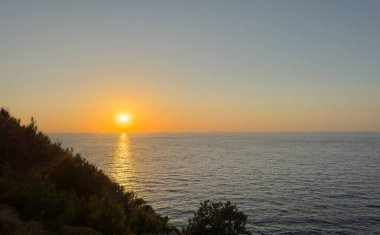 Sakin denizin üzerinde altın gün batımı ve gölgeli sahil kayalıkları