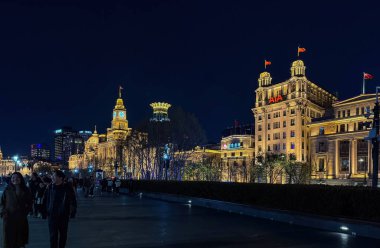 Şangay, Çin, 30 Mart 2025. Aydınlatılmış tarihi rıhtım binaları gece Bund boyunca parlıyor, insanlar geziniyor, arka planda modern kuleler var.