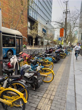 Şangay, Çin, 31 Mart 2025. Şehir merkezindeki kaldırımda, cam binalarda ve bulutlu gökyüzünde peş peşe bisikletleri ve motosikletleri paylaşırdık.
