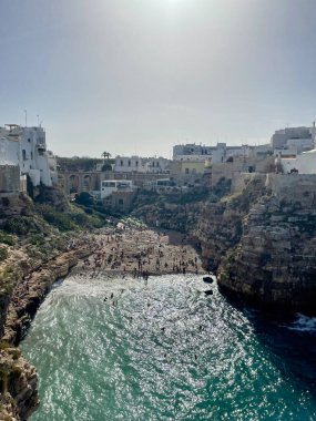 Polignano a Mare, İtalya, 20 Ekim 2023. Lama Monachile plajında turistler, uçurum kenarındaki beyaz evler ve turkuaz deniz suyu, yukarıdan manzara