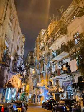 Napoli, İtalya, 17 Ekim 2023. Dar sokaklar geceleri aydınlık, balkonlu eski apartmanlar, çamaşırhaneler, park edilmiş arabalar.