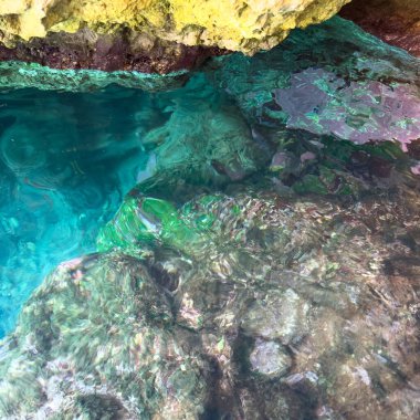 Yunanistan 'ın Korfu adası kıyı şeridindeki kayalık mağaranın altında berrak turkuaz deniz suyu parlatıcıları. Güneş ışığı sığ sularda yansıyor.