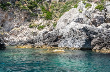 Berrak turkuvaz denizinden yükselen sarp kayalıklar, dalgalanan sulara yansıyan güneş ışığı, Korfu adası Yunanistan, Paleokastritsa
