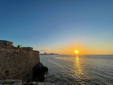 Havana, Küba 'daki antik kale duvarlarından okyanus manzaralı altın gün batımı. Sudaki yansımalar ve ufuktaki ufuk çizgisi