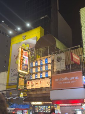 Bangkok, Tayland, 7 Kasım 2025. Neon Laoaire tabelası ve kağıt fenerler gece kalabalık bir Bangkok caddesinde, vitrin ışıkları ve reklam panoları