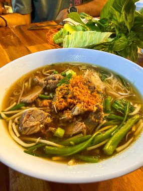 Tayland, Ao Nang, 31 Ekim 2025. Tahta bir restoran masasında sebzeli erişte çorbası ve çıtır çıtır sarımsak..