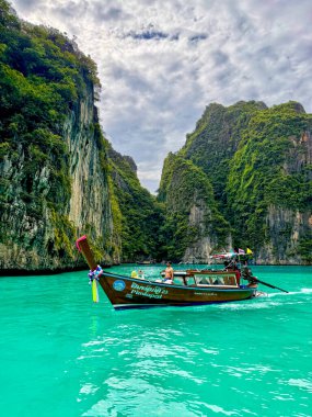 Ko Phi Phi, Tayland, 3 Kasım 2025. Uzun kuyruklu tekne turkuaz gölde, kireçtaşı kayalıklarının altında, bulutlu gökyüzünde, sakin tropikal sularda.