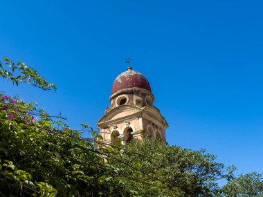 Yunanistan 'ın Korfu adasındaki yemyeşil yemyeşil yemyeşil üzerinde kırmızı kubbesi olan kilise çan kulesi yükseliyor. Eski kasabadaki Tenedos Manastırı.