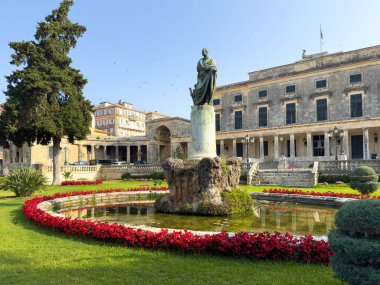 Korfu, Yunanistan, St. Michael ve St. George Sarayı 'nın önündeki bronz heykel, bir çeşme ve kırmızı renkli çiçeklerle çevrili, açık mavi gökyüzü.