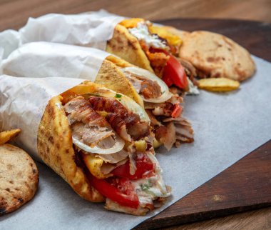 Kızarmış et, soğan, domates ve tzatziki ile doldurulmuş döner jiroskoplar ya da shawarma paketleri, yakın plan, geleneksel sokak yemekleri.