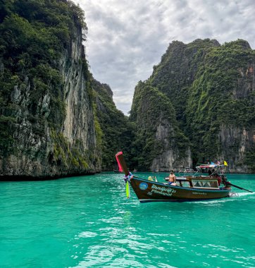 Ko Phi Phi, Tayland, 3 Kasım 2025. Uzun kuyruklu tekne turkuaz gölde, kireçtaşı kayalıklarının altında, bulutlu gökyüzünde, sakin tropikal sularda.
