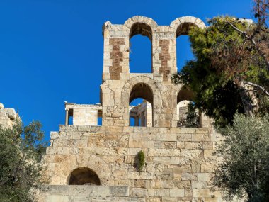 Herodes Atticus 'lu Odeon, Yunanistan' ın Atina kentindeki Akropolis tepesindeki yeşil ağaçların üzerinde Herodeion taşı kalıntıları yükseliyor. Mavi gökyüzü