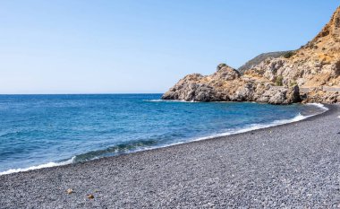 Chios Adası, Yunanistan. Mavra Volia Sahili, siyah çakıl taşı sahili. Engebeli kayalıkların altında hafif dalgalar, mavi gökyüzü, güneşli yaz günü.