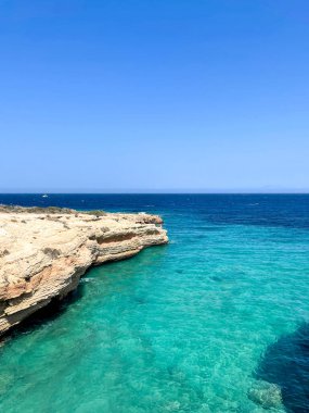 Cyclades adaları, Yunanistan. Koufonisia yakınlarındaki turkuaz denizin üzerindeki kayalıklar. Temiz sığ su, uzak yelkenli, mavi gökyüzü.