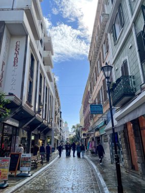 Cebelitarık, Birleşik Krallık, 10 Mart 2025. Yağmurdan, dükkanlardan, tarihi binalardan, yürüyen insanlardan, mavi gökyüzünden sonra kaldırım taşı bir cadde.