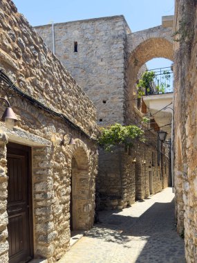 Chios Adası, Yunanistan. Mesta Ortaçağ köyündeki dar kaldırım taşı sokağı. Geleneksel mimari taş evler ve kemerler. Kırsal ahşap kapılar ve fenerler