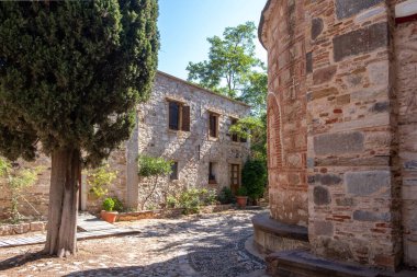 Yunanistan 'ın Chios Adası' ndaki Nea Moni manastırı avlusundaki taş duvar binaları. Ağaçlar ve seramik saksılar, mavi gökyüzü.